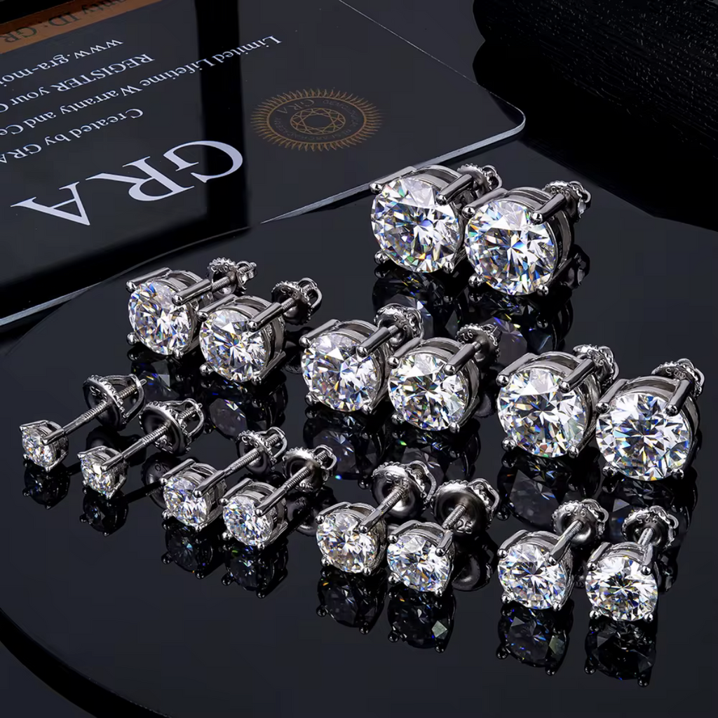 Round moissanite studs in several sizes on a black surface with a GRA card