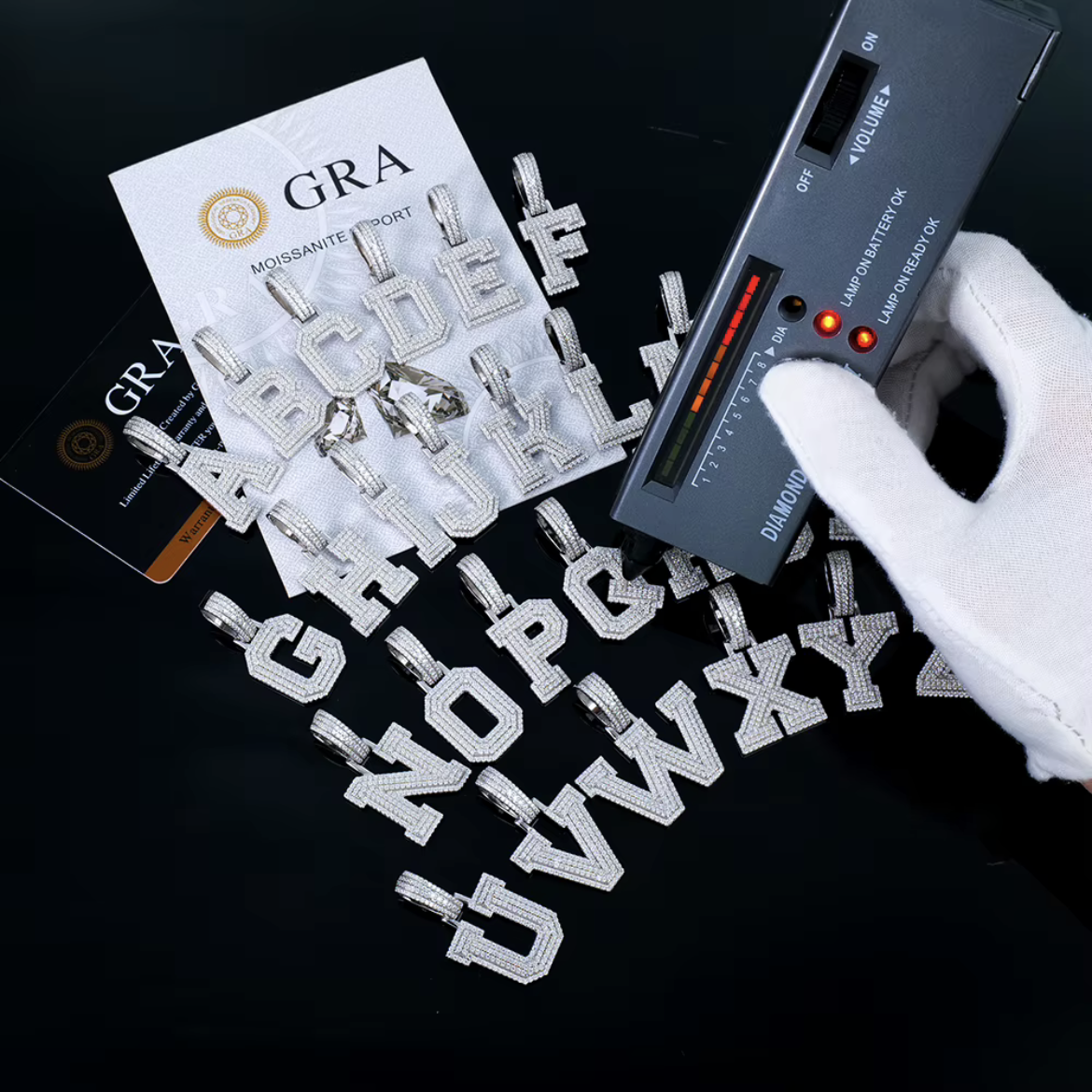 Moissanite initial letters with a GRA report card and a handheld gem tester